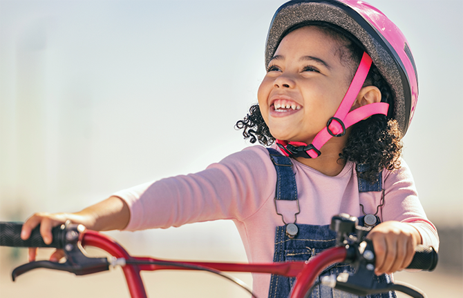little girl wearing a pink helmet riding a bike